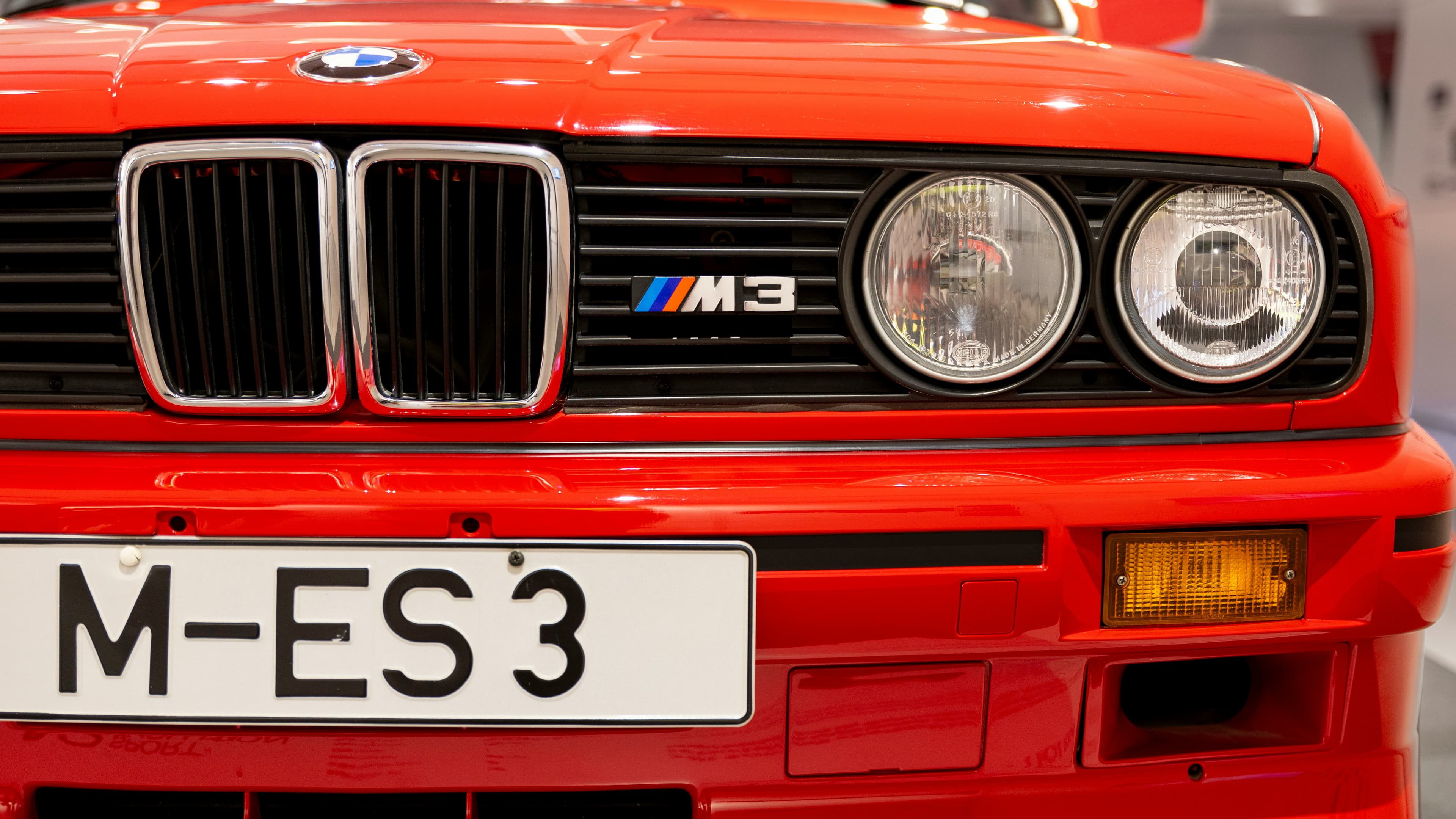 Red BMW M3 E30 front-end detail with kidney grille, M3 badge and round headlights