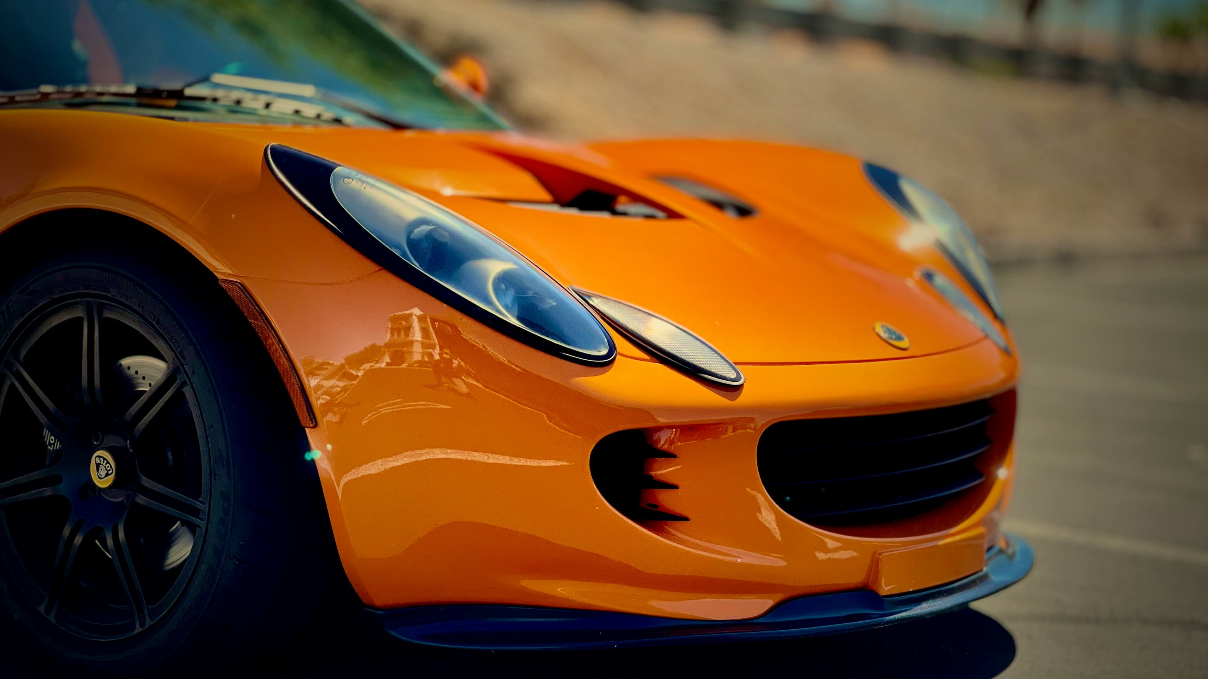 Orange Lotus Elise front-end detail showing its sculpted nose, headlight and Lotus badge
